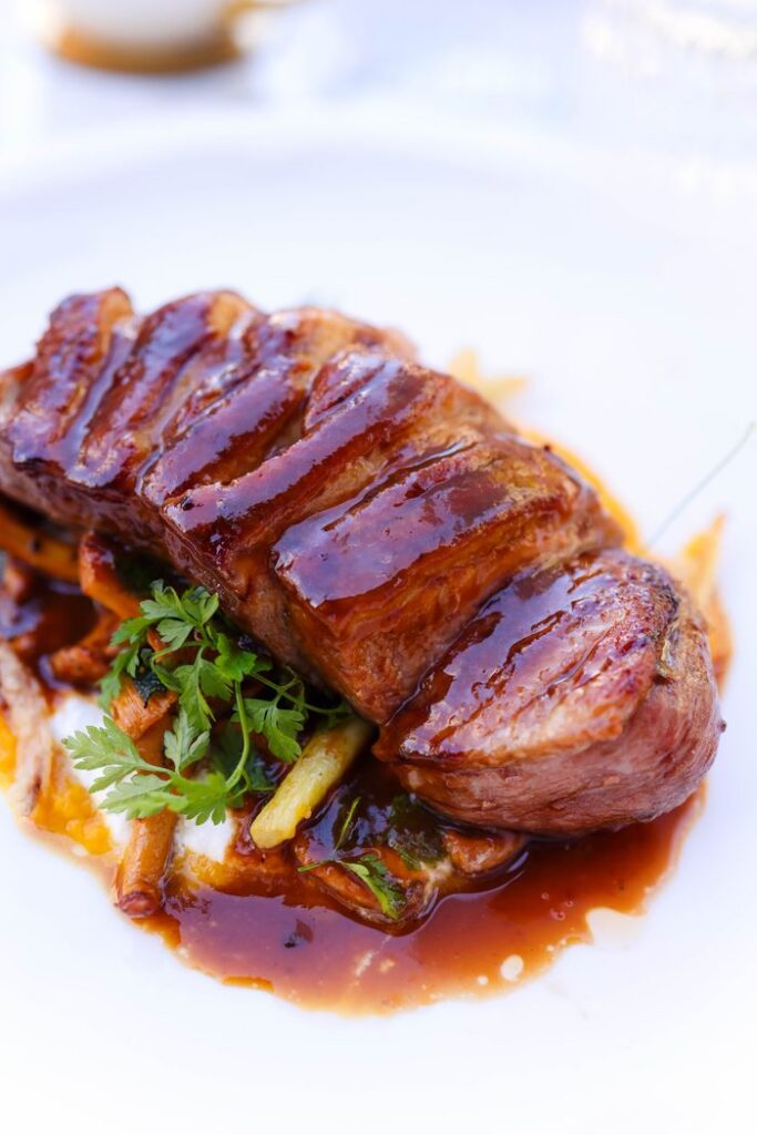Close-up of a glazed beef steak served with garnish on a white plate.