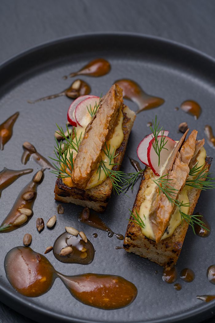 Elegant presentation of smoked fish on bread with creamy sauce and garnish.