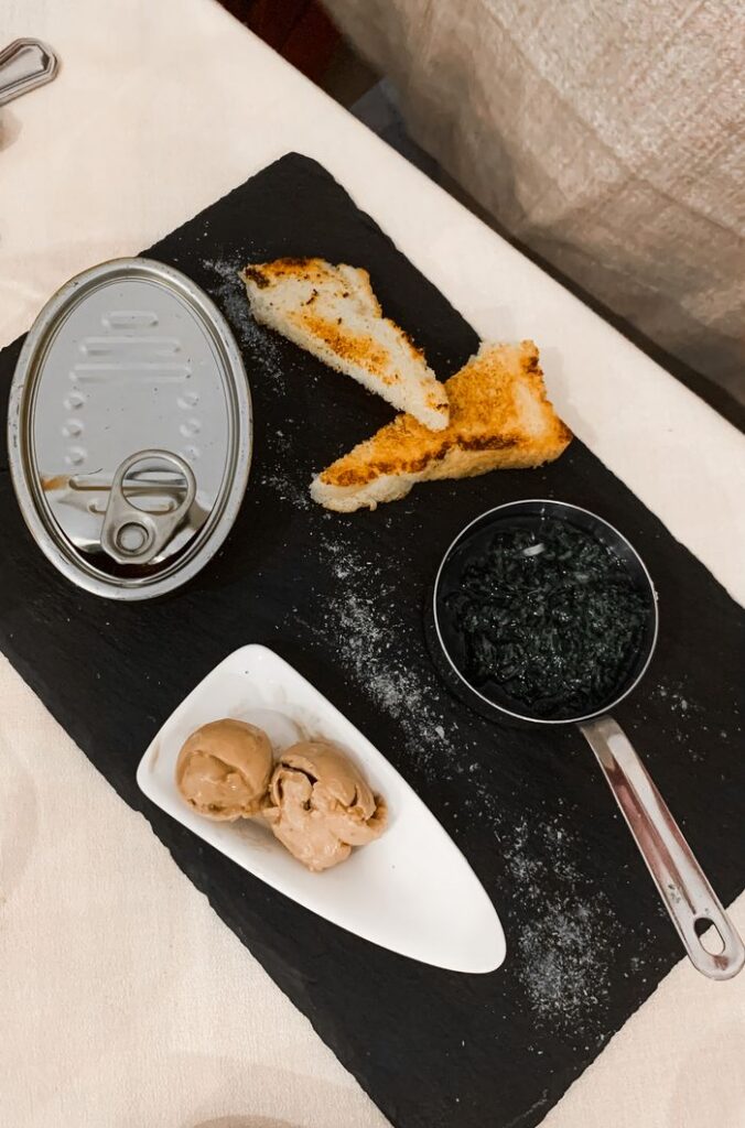 Elegant appetizer with fish can, bread toast, and spices on a black slate board.